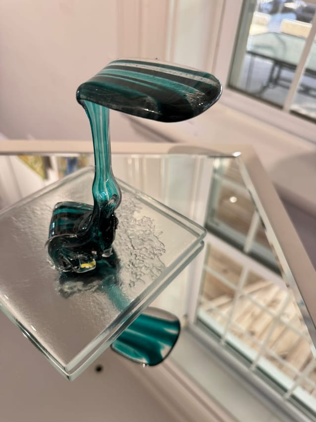 Teal glass sculpture flowing like a waterfall from a striped glass top down to a glass base